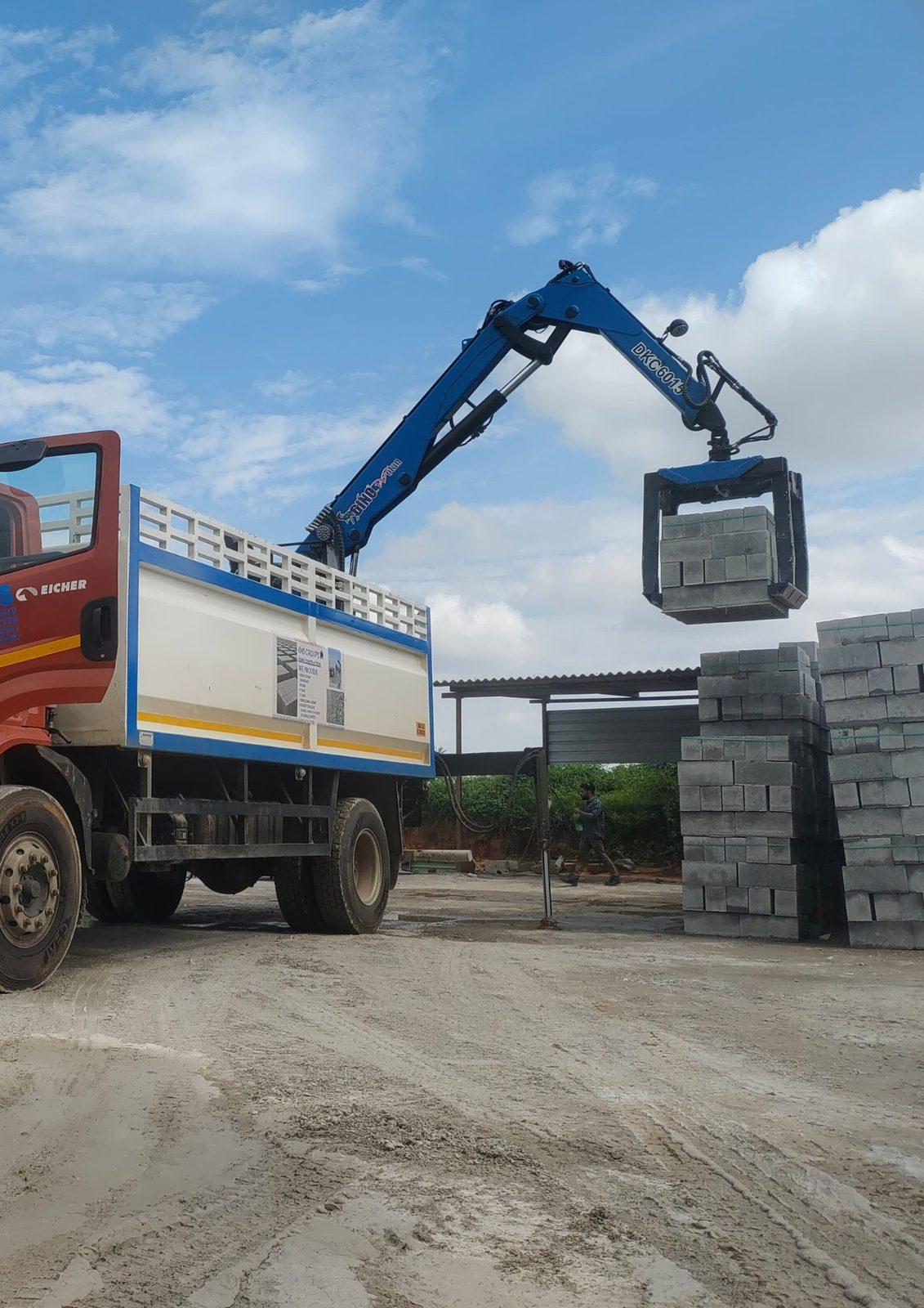 Knuckle boom truck-mounted crane lifting a stack of blocks at a block yard